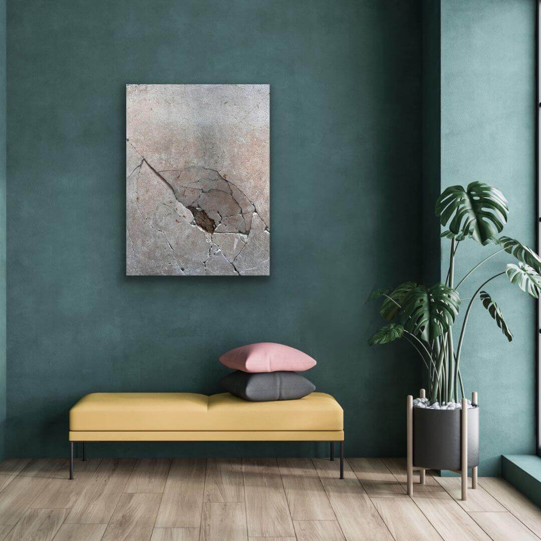 Detailfotografie eines zerbrochenen Betonwürfels an petrolfarbener Wand über einem gelben Sitzmöbel